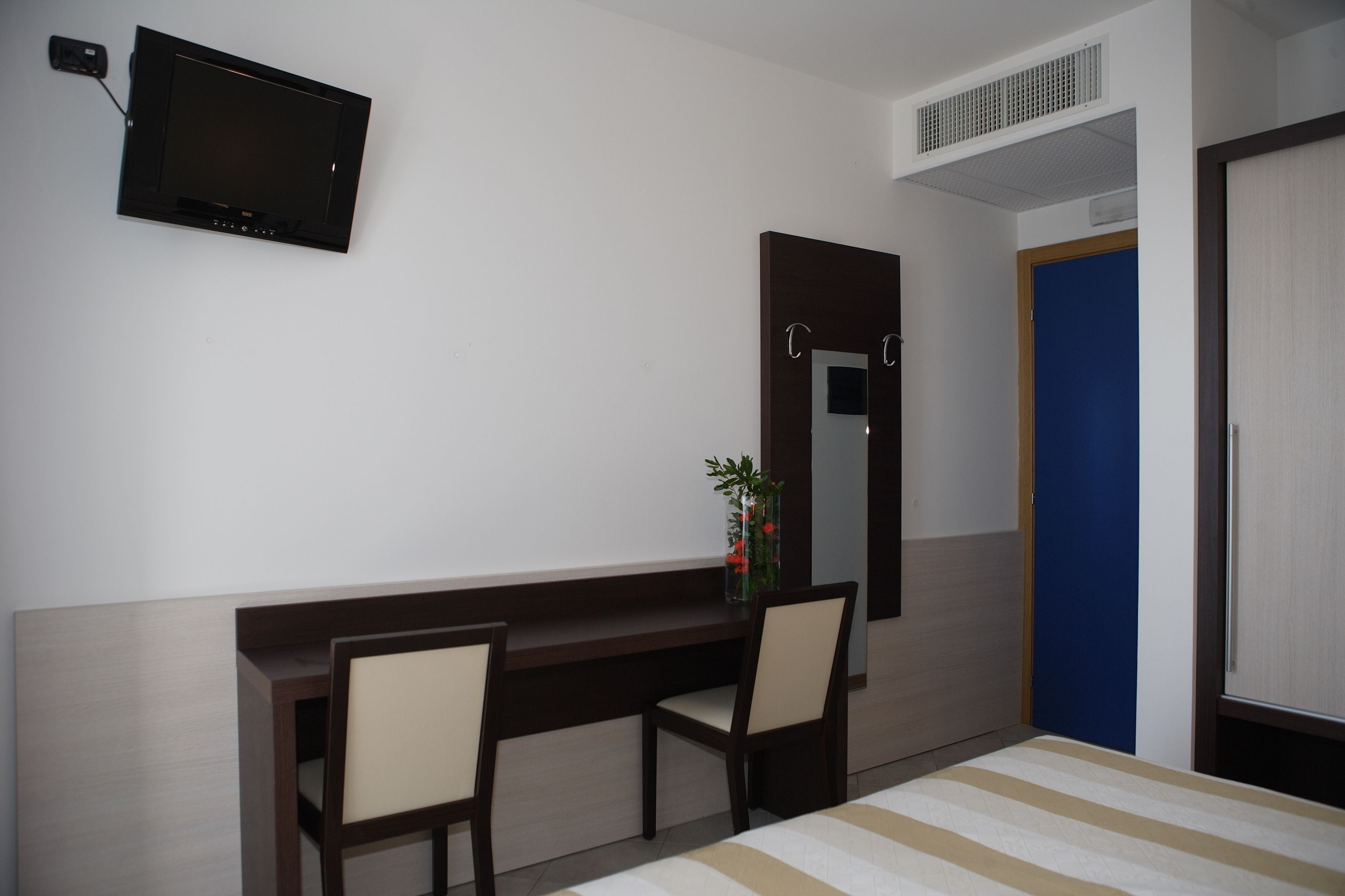 A hotel room with a bed, a desk with two chairs, a television mounted on the wall, a mirror, and a door.