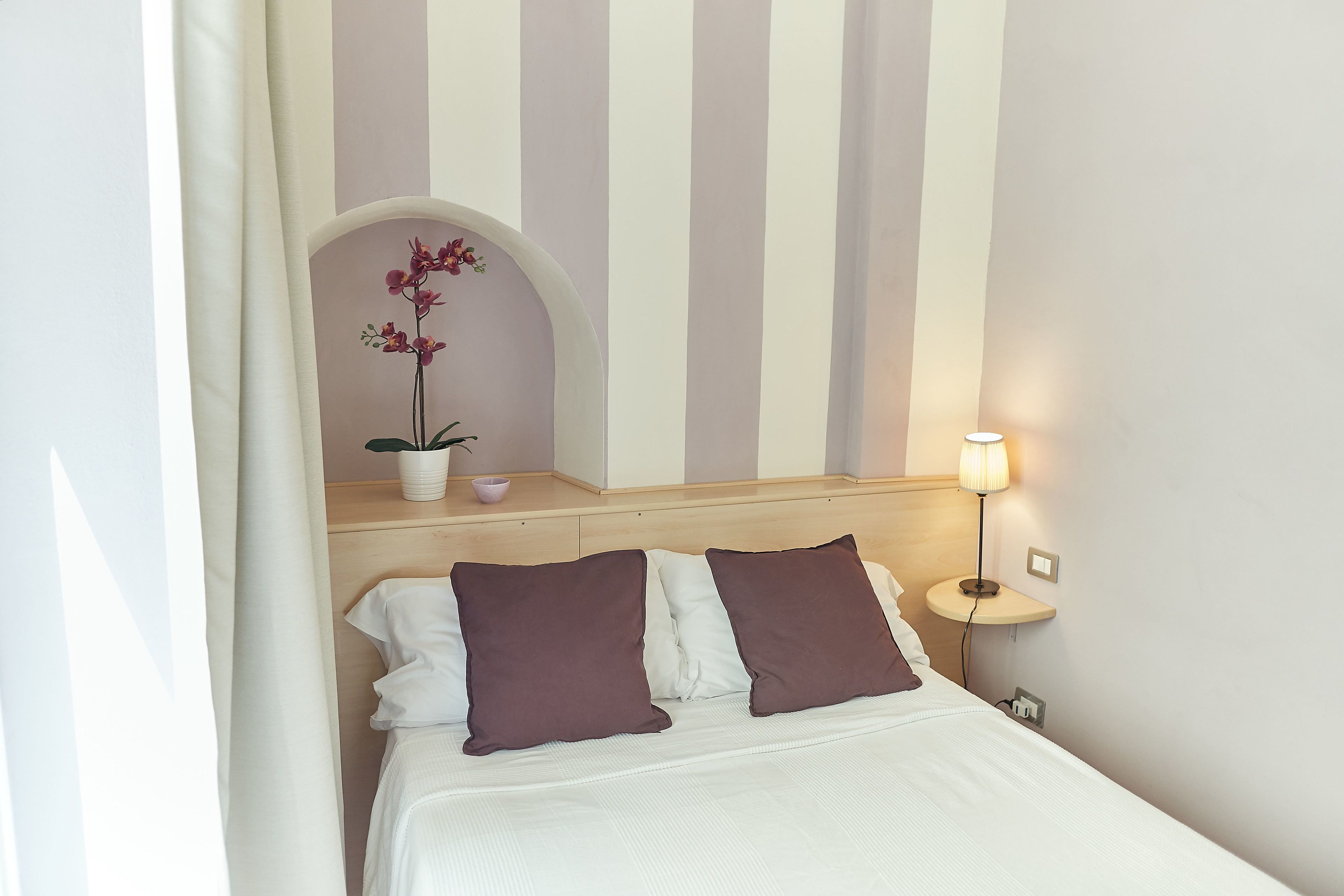 A neatly made bed with two pillows, a bedside lamp, and a small potted orchid on a bedside table.