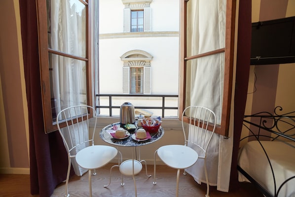 A balcony with a table set for two, a kettle, and a basket of items.