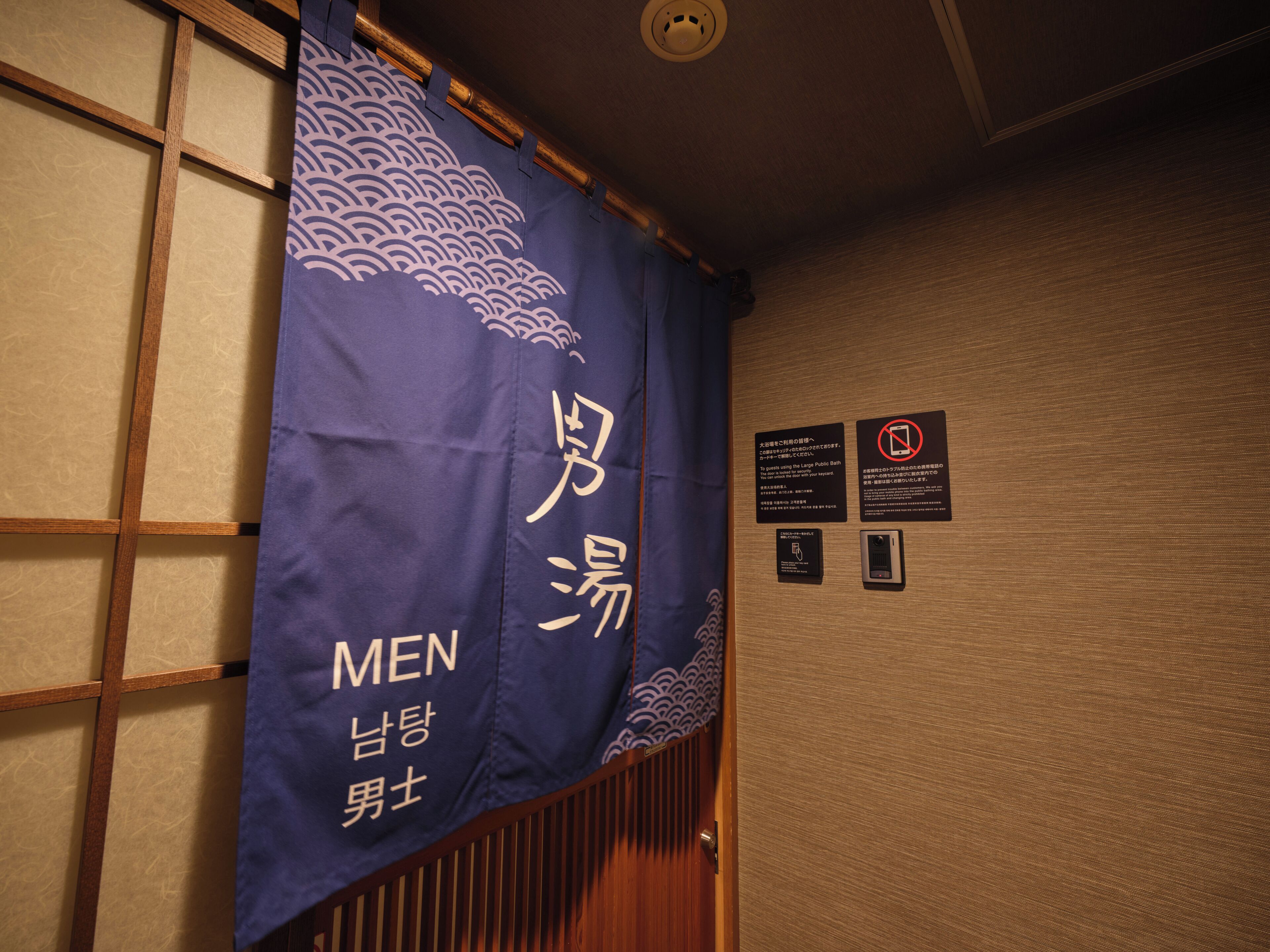 A room with a wooden sliding door, a blue curtain with Japanese characters, and a wall-mounted sign with instructions.
