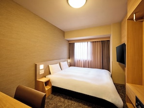 Ein Hotelzimmer mit einem großen Bett, einem Nachttisch, einem Sessel, einem Flachbildfernseher und einem Fenster mit Vorhängen.