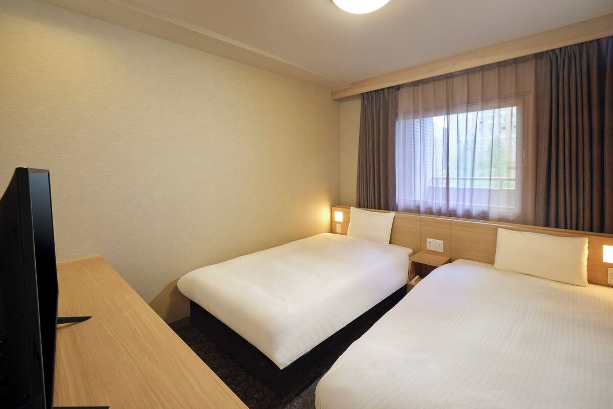 A hotel room with two beds, a TV, and a window with curtains.