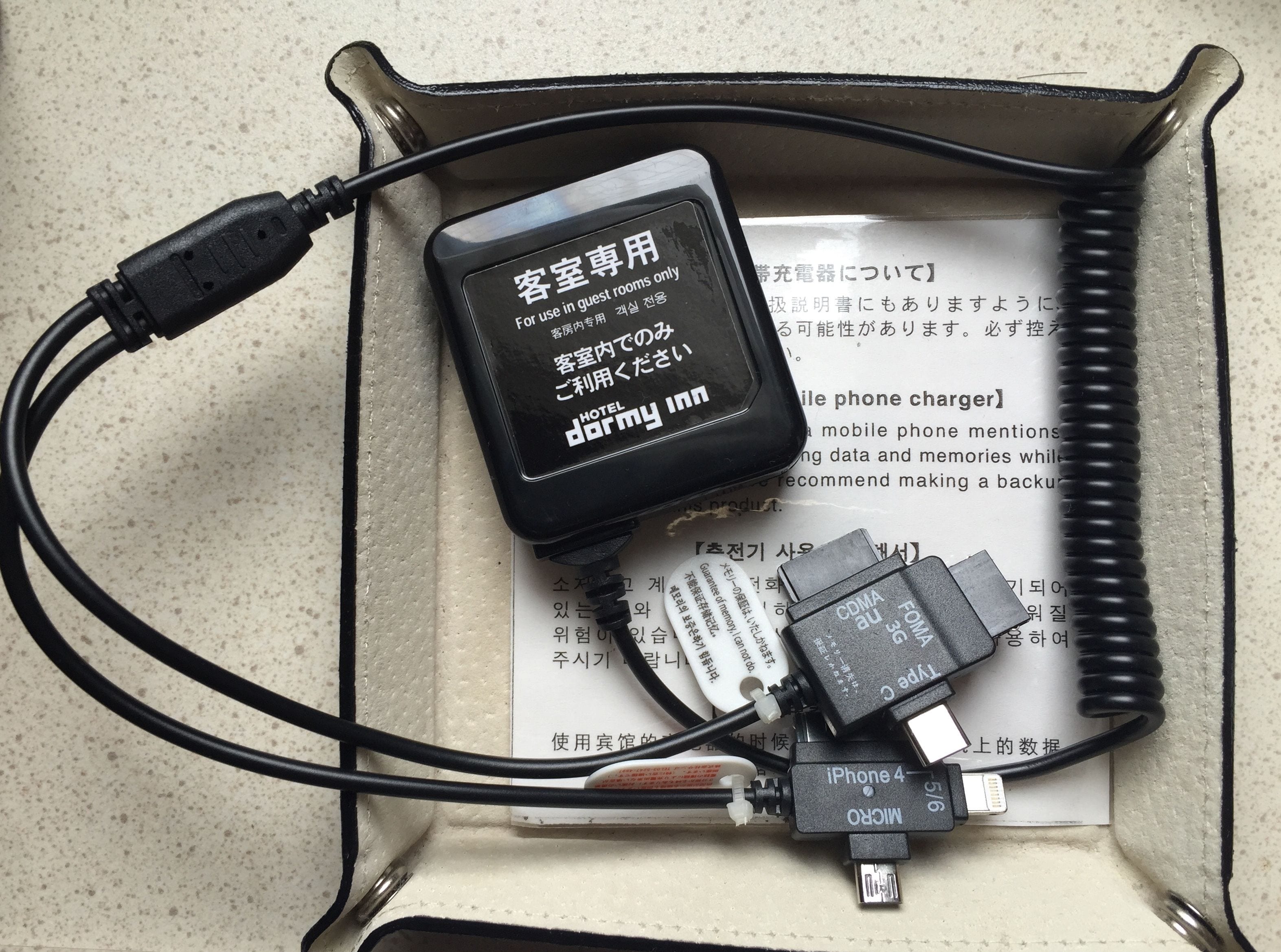 A hotel room with a black power adapter, a micro USB cable, and a USB-C cable connected to a device.