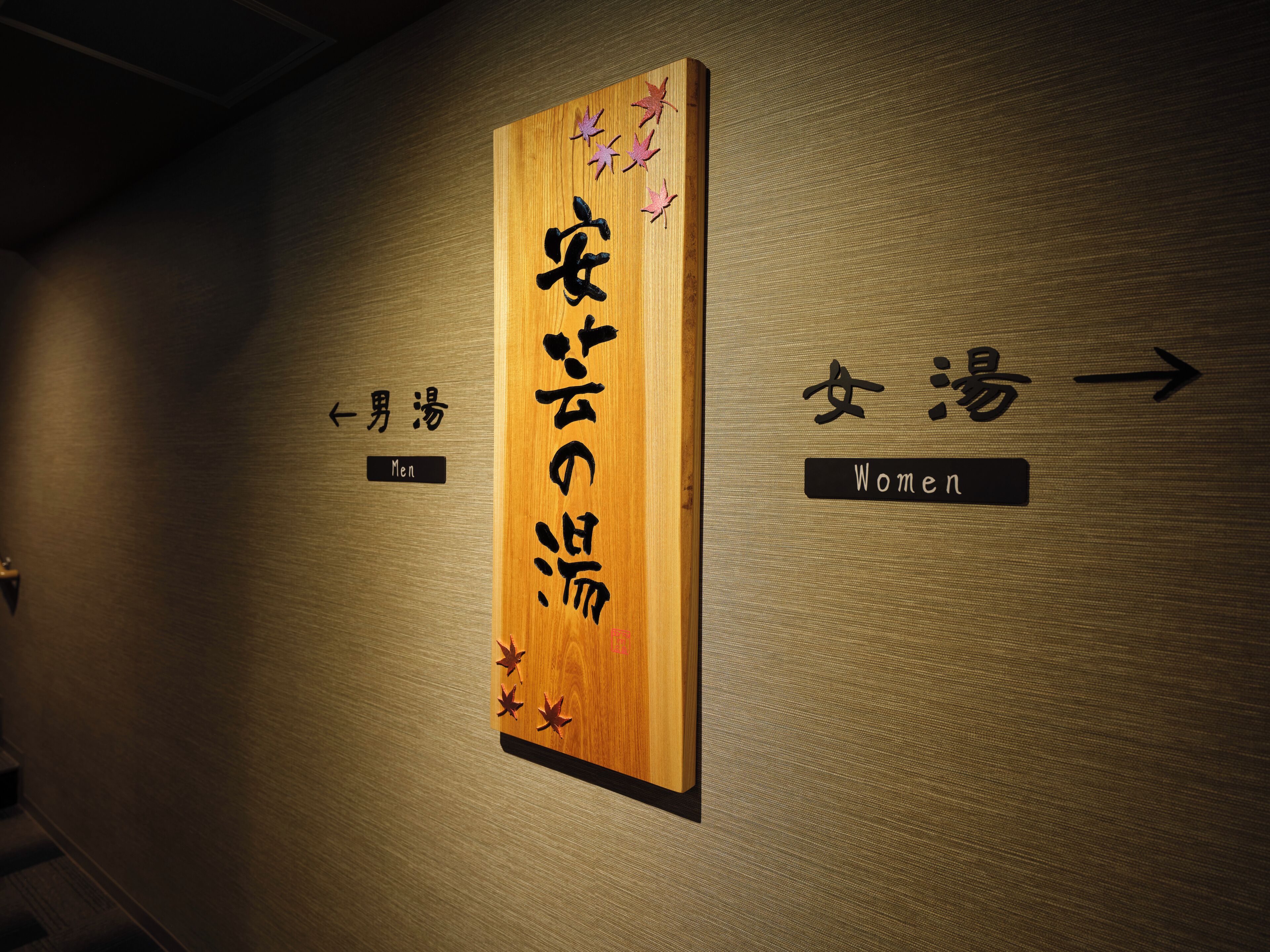 Un letrero de madera con caracteres japoneses y flechas que indican indicaciones para hombres y mujeres.
