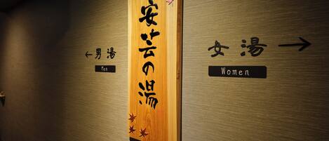 Un letrero de madera con caracteres japoneses y flechas que indican indicaciones para hombres y mujeres.