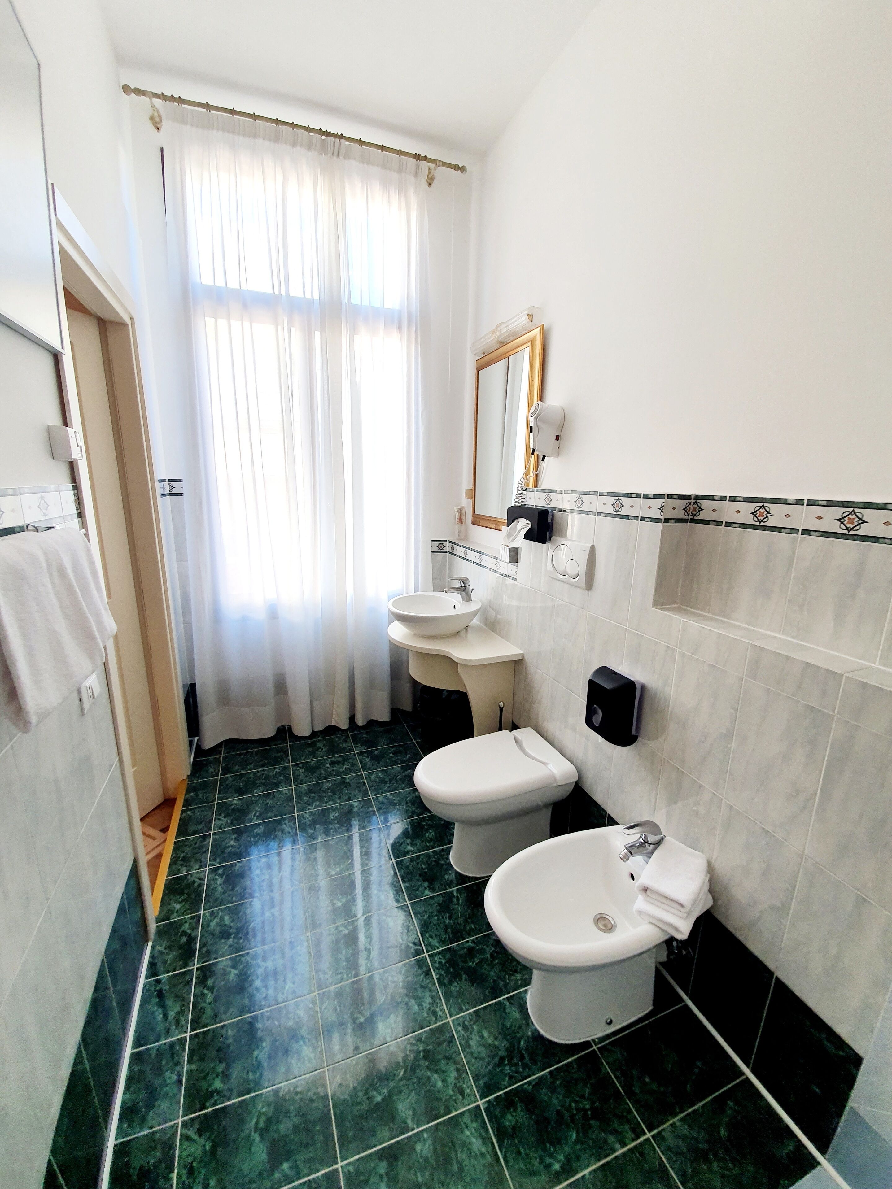 Een badkamer met toilet, bidet en wastafel, een spiegel en een handdoekhouder.