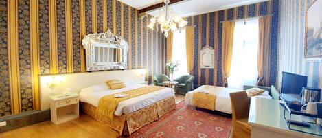 A hotel room with two beds, a large mirror, a chandelier, a desk with a computer, and a TV.
