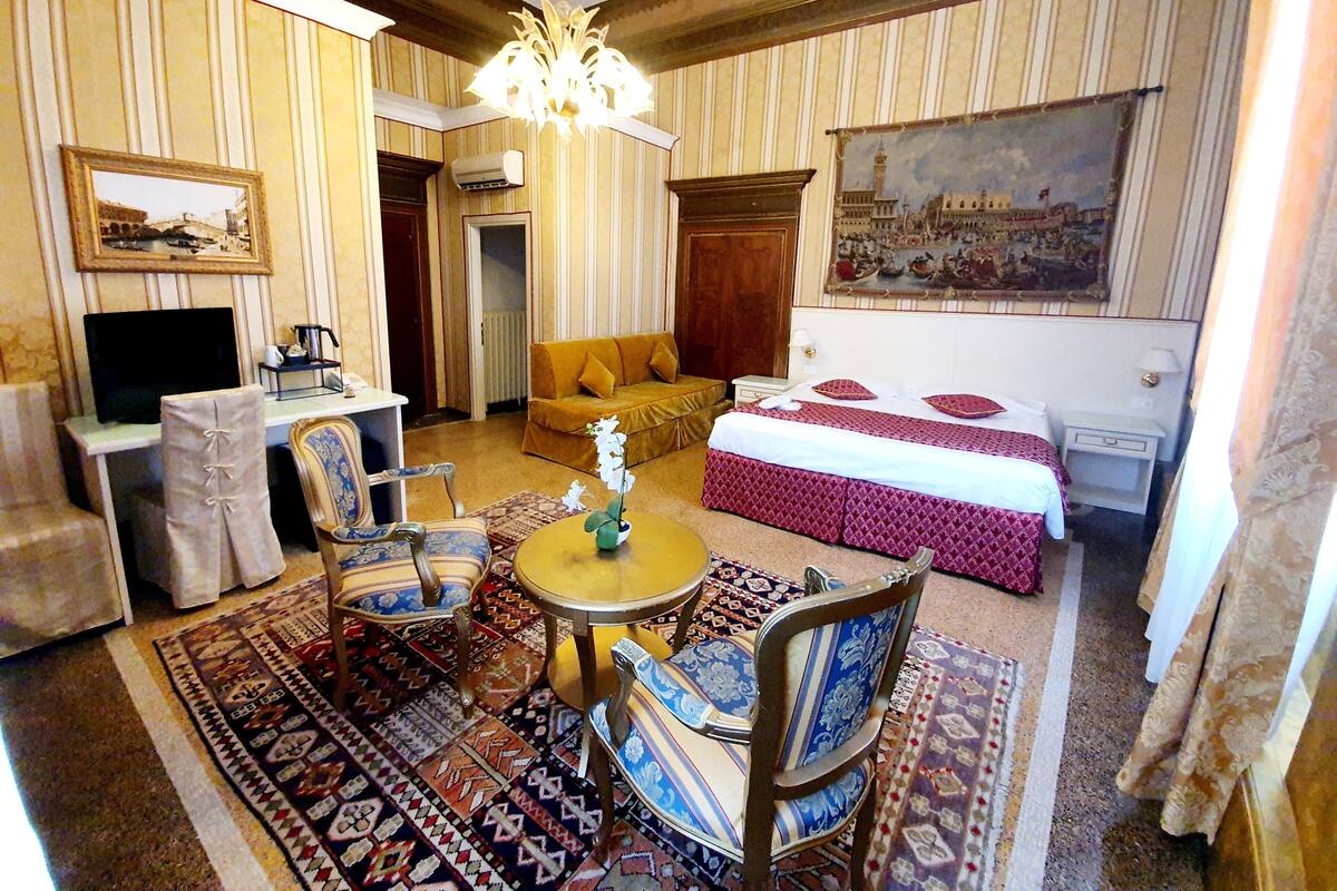 Habitación de hotel con cama, sofá, escritorio con computadora, televisor y candelabro.