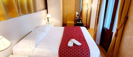 A hotel room with a bed, bedside table, lamp, and a red patterned rug.