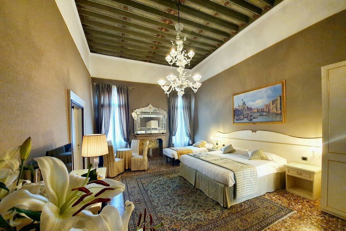 Una habitación de hotel con una cama grande, una araña, una chimenea y un cuadro de paisaje urbano en la pared.