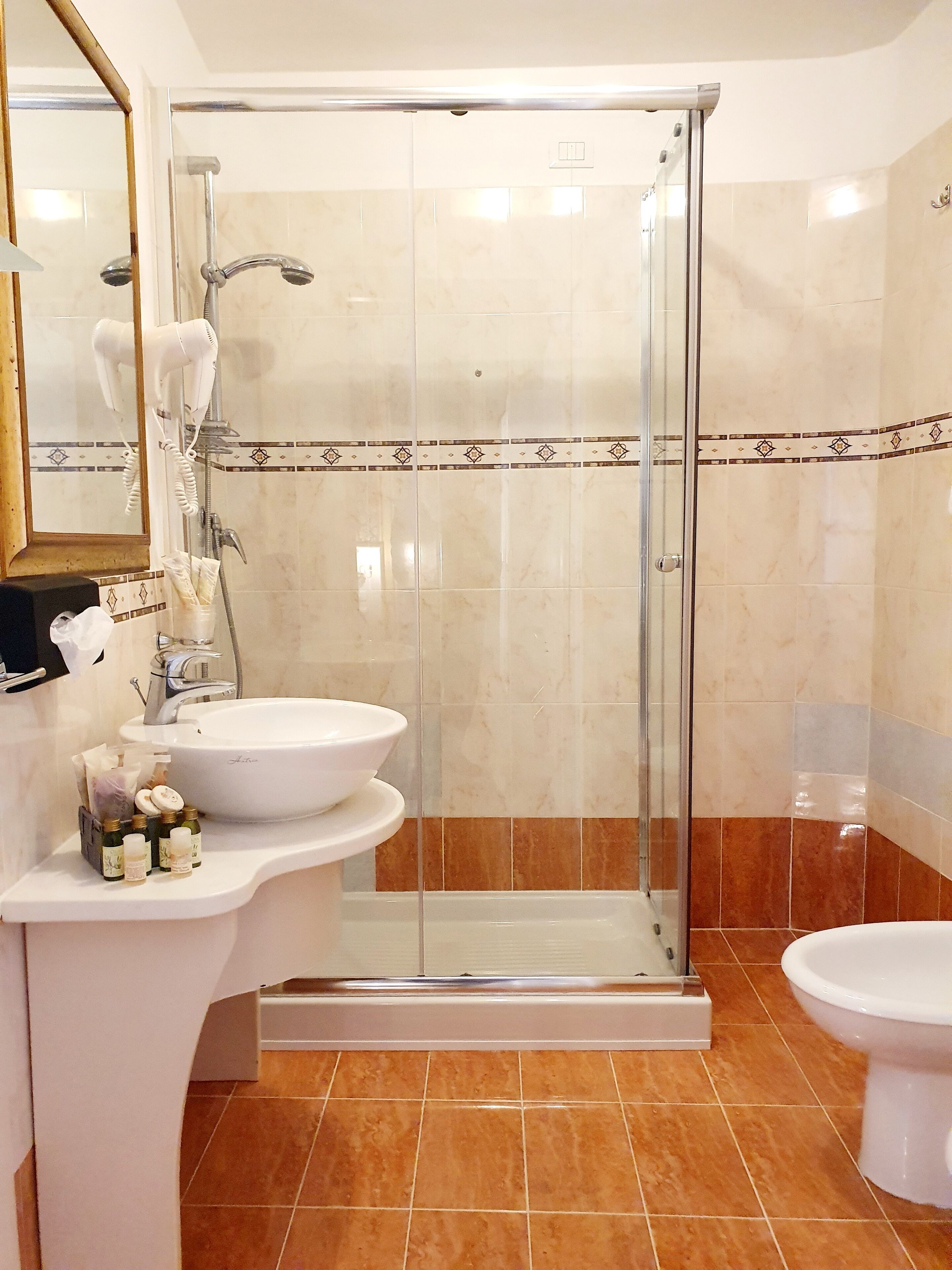 A bathroom with a glass-enclosed shower, a sink with toiletries, and a toilet.