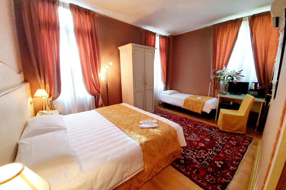 Habitación de hotel con una cama grande, una cama más pequeña, un escritorio con una silla, un armario y un televisor.
