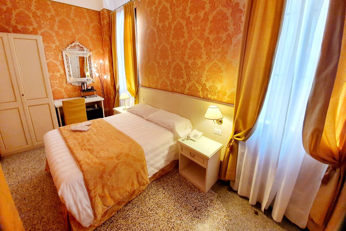 Una habitación de hotel con una cama grande, un escritorio con lámpara, un espejo y cortinas.