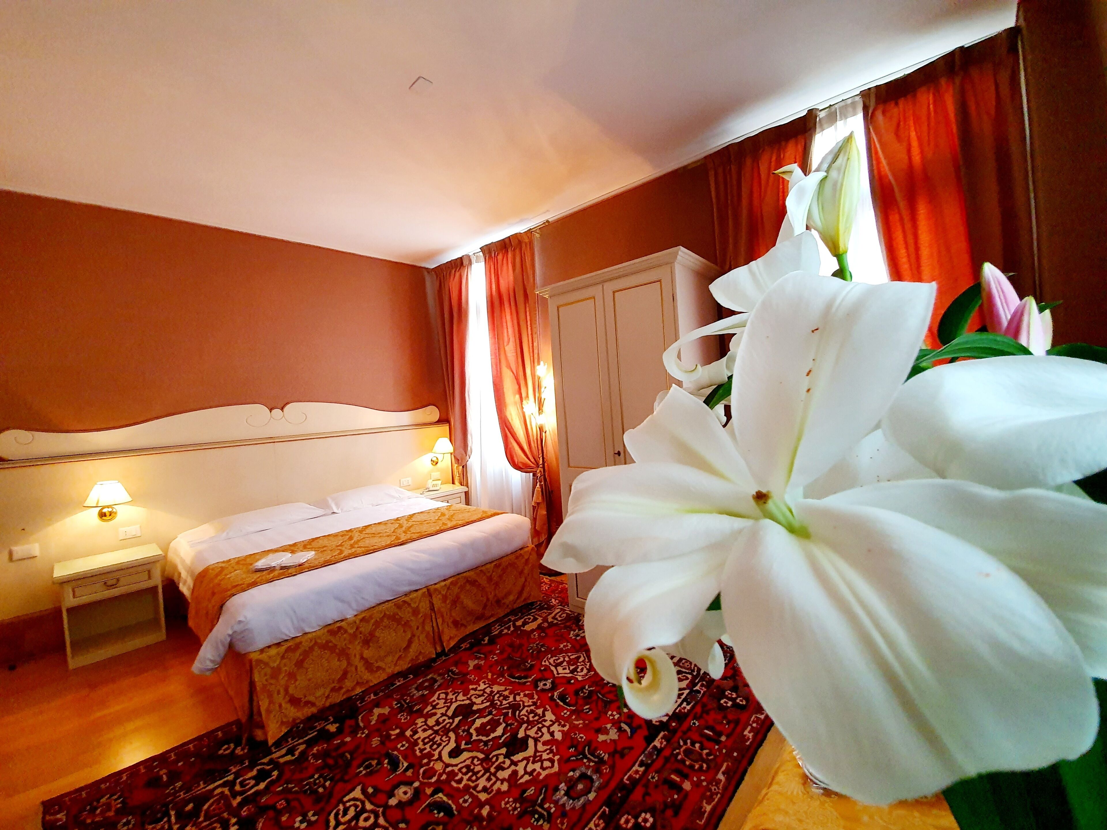 A hotel room with a bed, bedside table, lamp, and a large white flower.