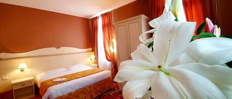 A hotel room with a bed, bedside table, lamp, and a large white flower.