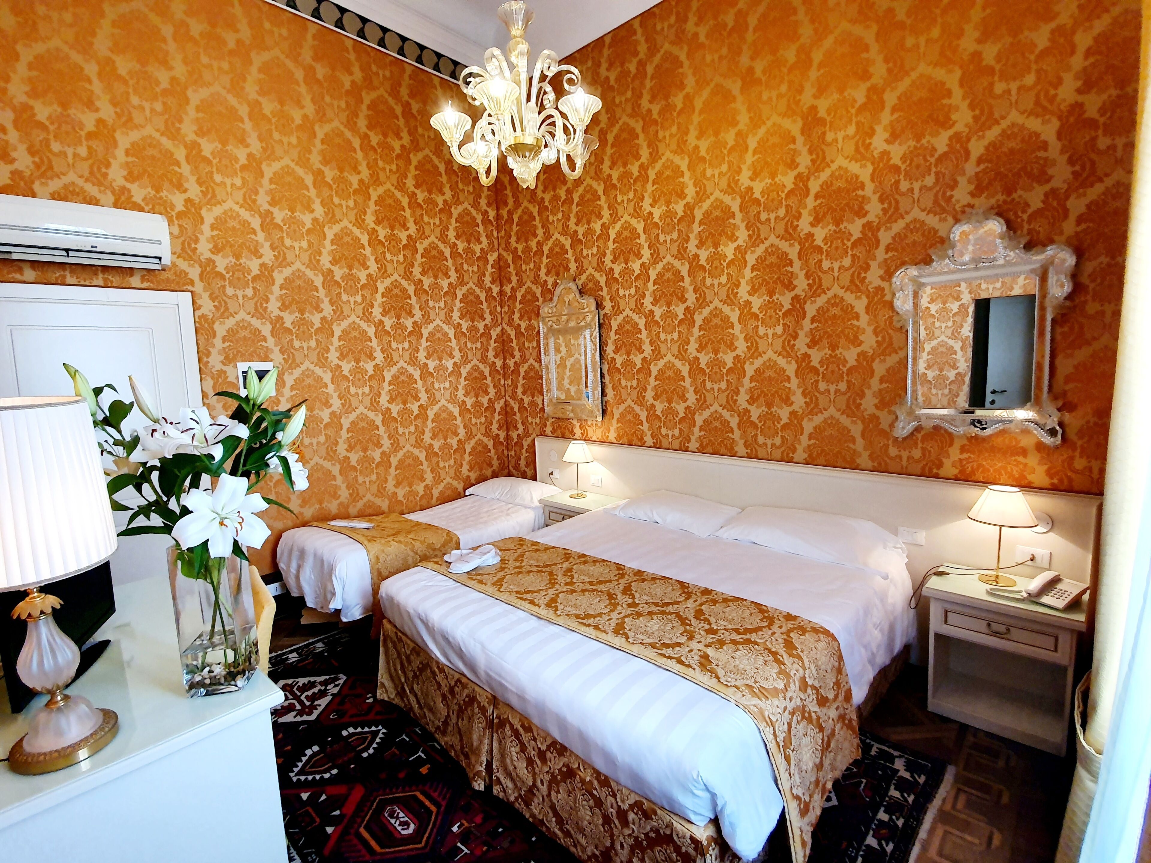 Une chambre d’hôtel avec deux lits, un lustre, un miroir et une table de chevet avec une lampe.
