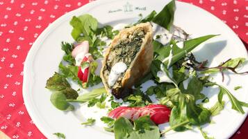A plate with a pastry, greens, and radishes on a tablecloth.