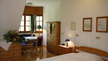 A bedroom with a bed, a wooden dresser, a desk with a chair, and a window with curtains.