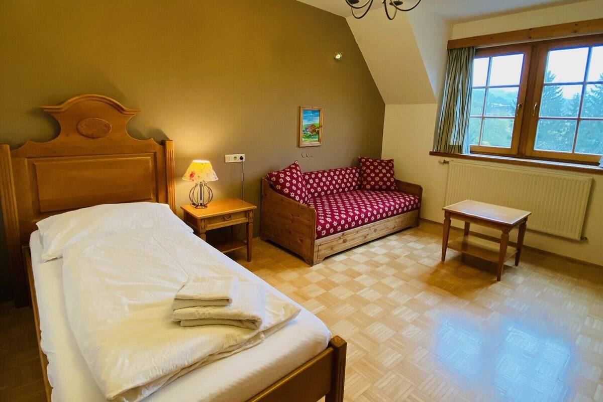 Un dormitorio con una cama de madera, un sofá rojo, una mesita y una ventana con cortinas.