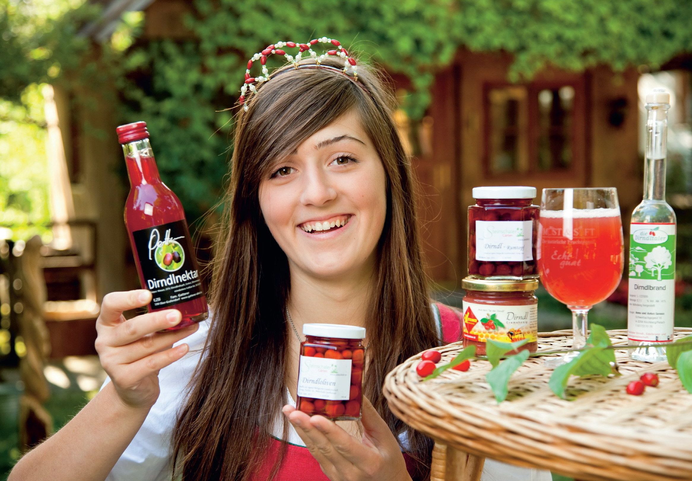 A person holding a bottle of Dindlnekta, a jar of Dindlnekta, and a glass of Dindlnekta on a table with a wicker tablecloth.