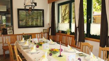 Un comedor con una mesa larga dispuesta para una comida, sillas de madera, una araña y una ventana con cortinas.