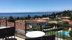 Un balcón con vista al mar, una piscina y edificios con tejados de teja.