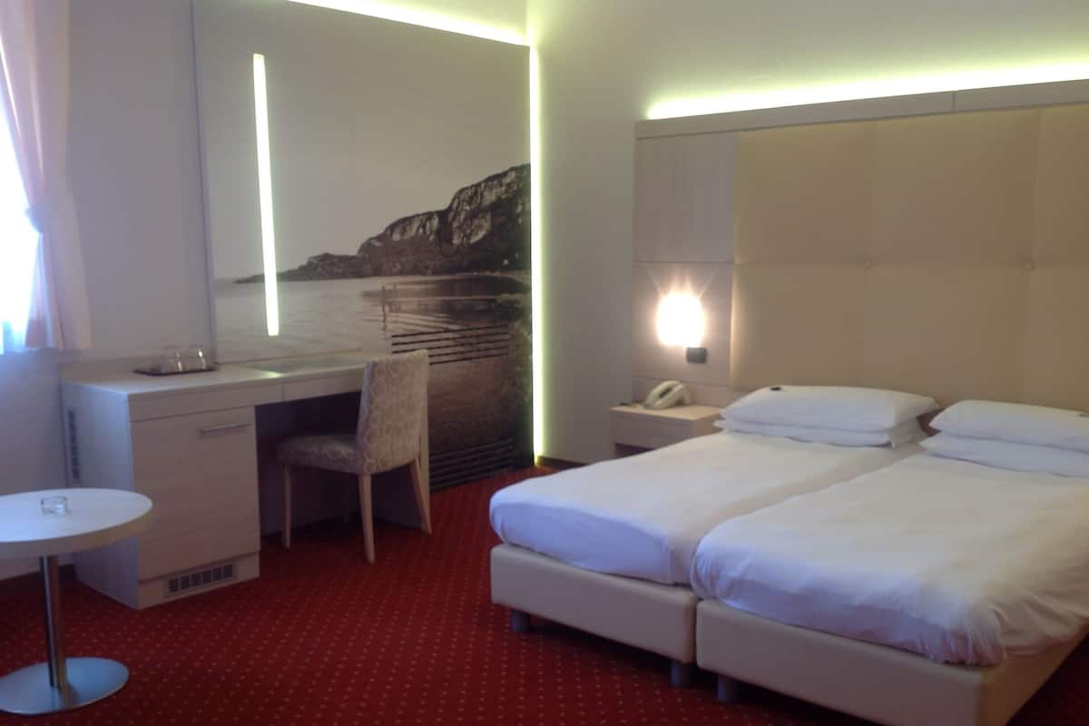 A hotel room with a desk, chair, two beds, a small table, and a nightstand with a phone.