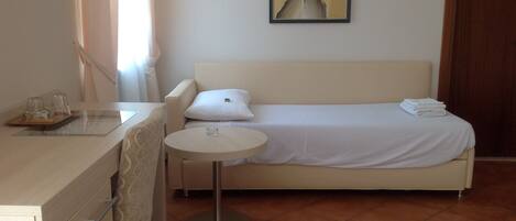 Quarto de hotel com cama, mesa redonda pequena, escrivaninha e cadeira, e um quadro na parede.