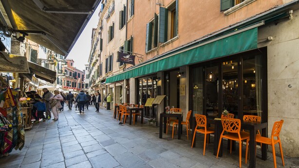 Una calle estrecha con mesas al aire libre y comercios.