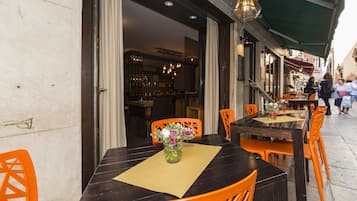 An outdoor dining area with tables and chairs, a vase with flowers, and a view of the street.