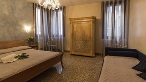 Una habitación de hotel con una cama, un aparador, una lámpara de araña y una ventana con cortinas.