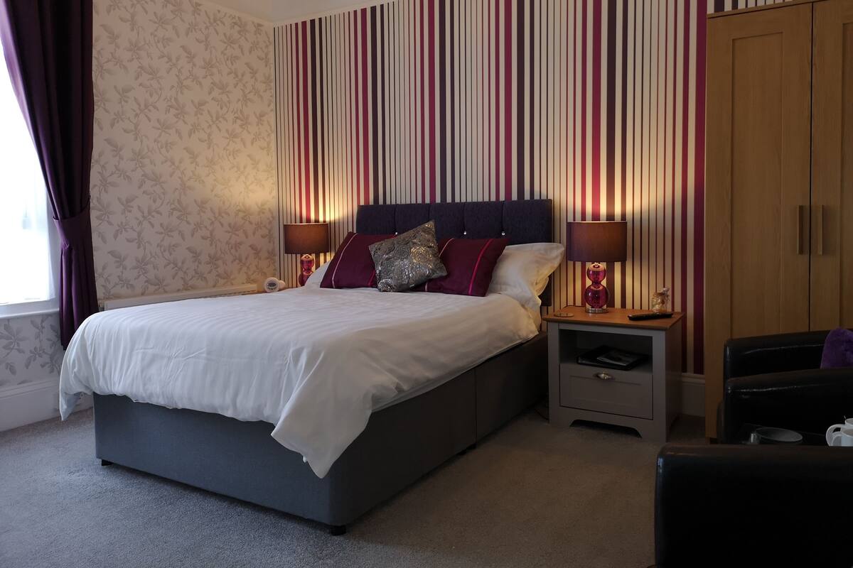 A bedroom with a bed, nightstands, a wardrobe, and a window with curtains.