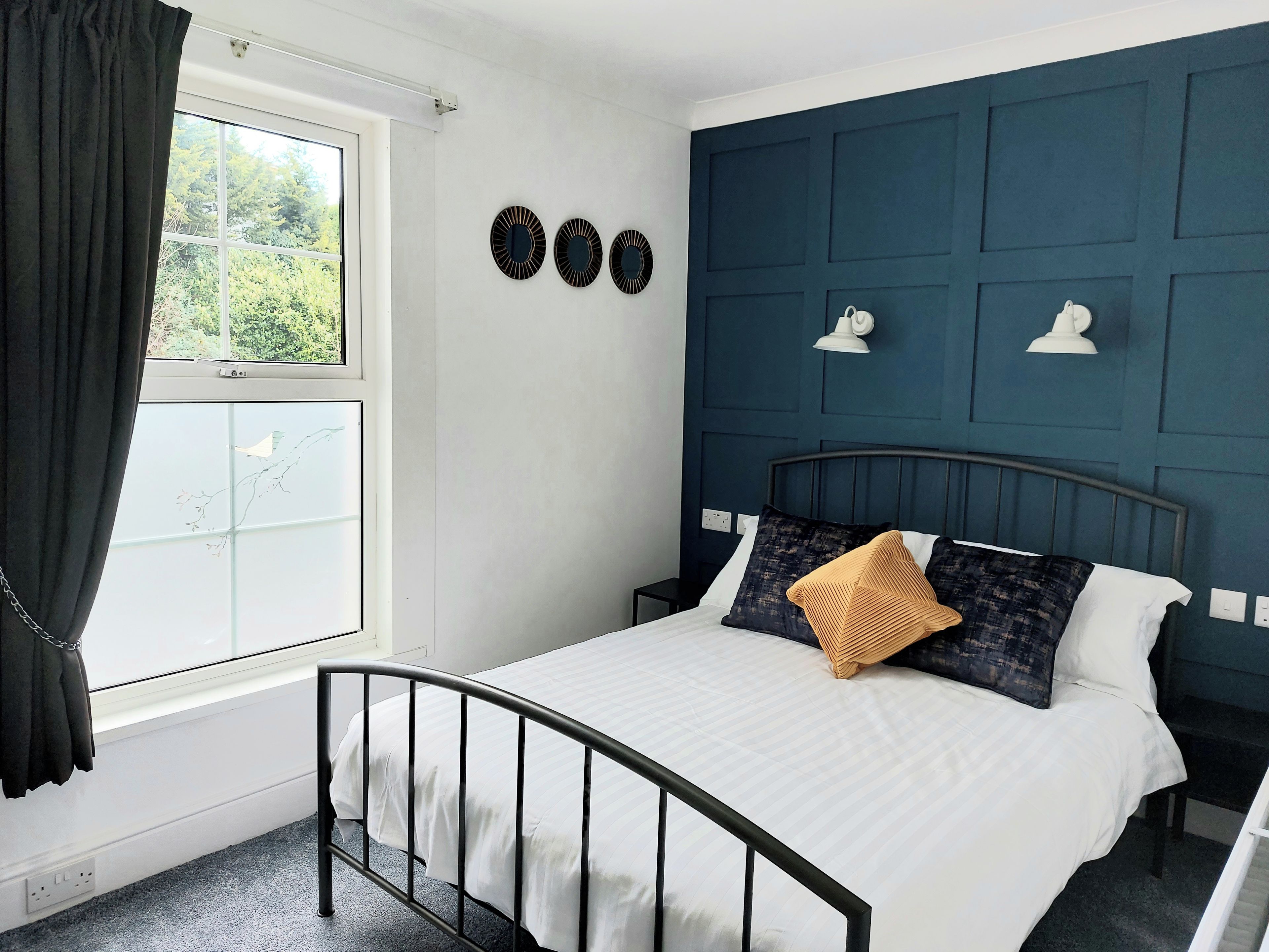 A bedroom with a bed, a window with curtains, a wall with decorative plates, and a blue accent wall.