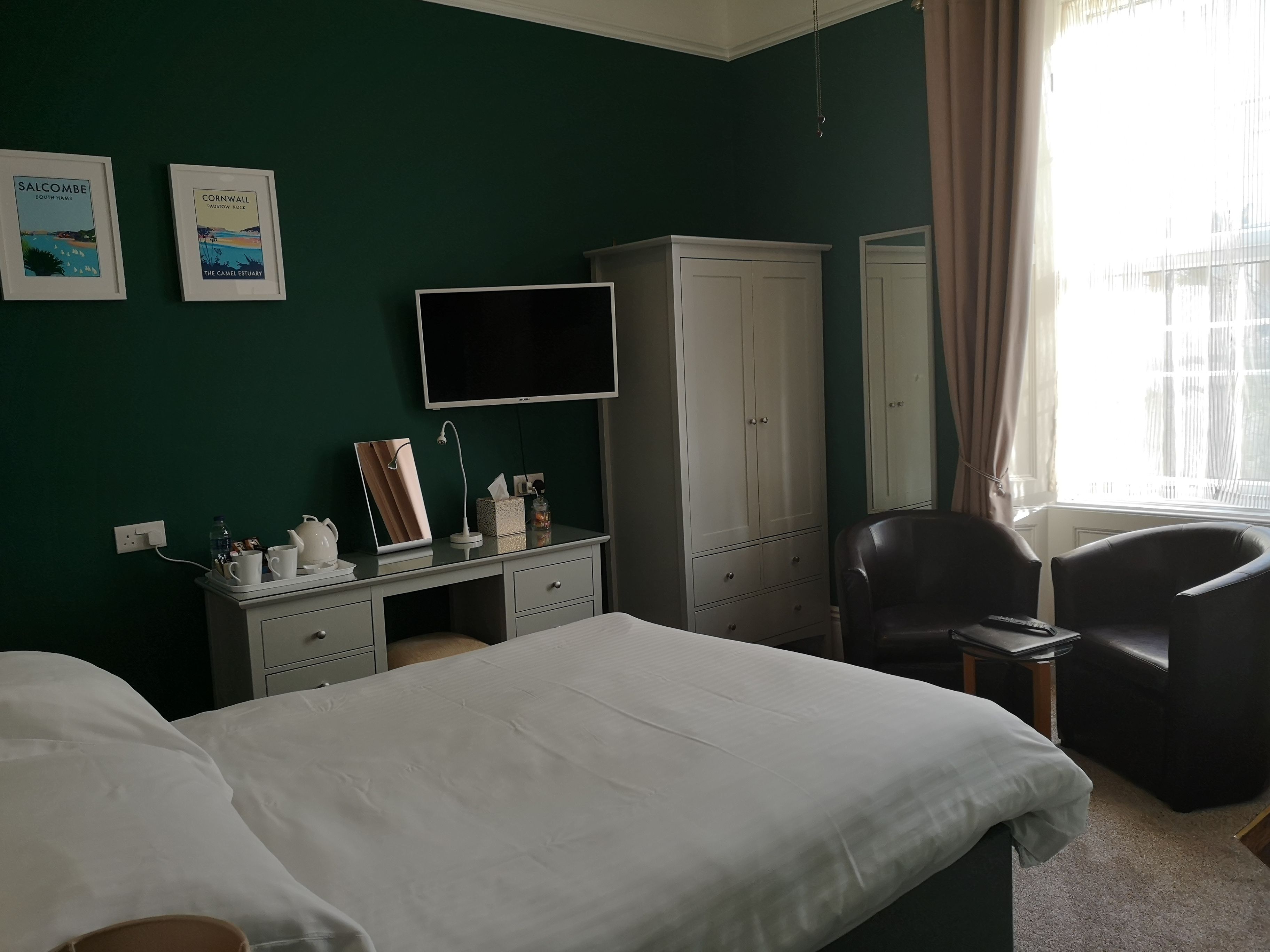 Una habitación de hotel con una cama, un escritorio con espejo, una silla, un armario y un televisor.