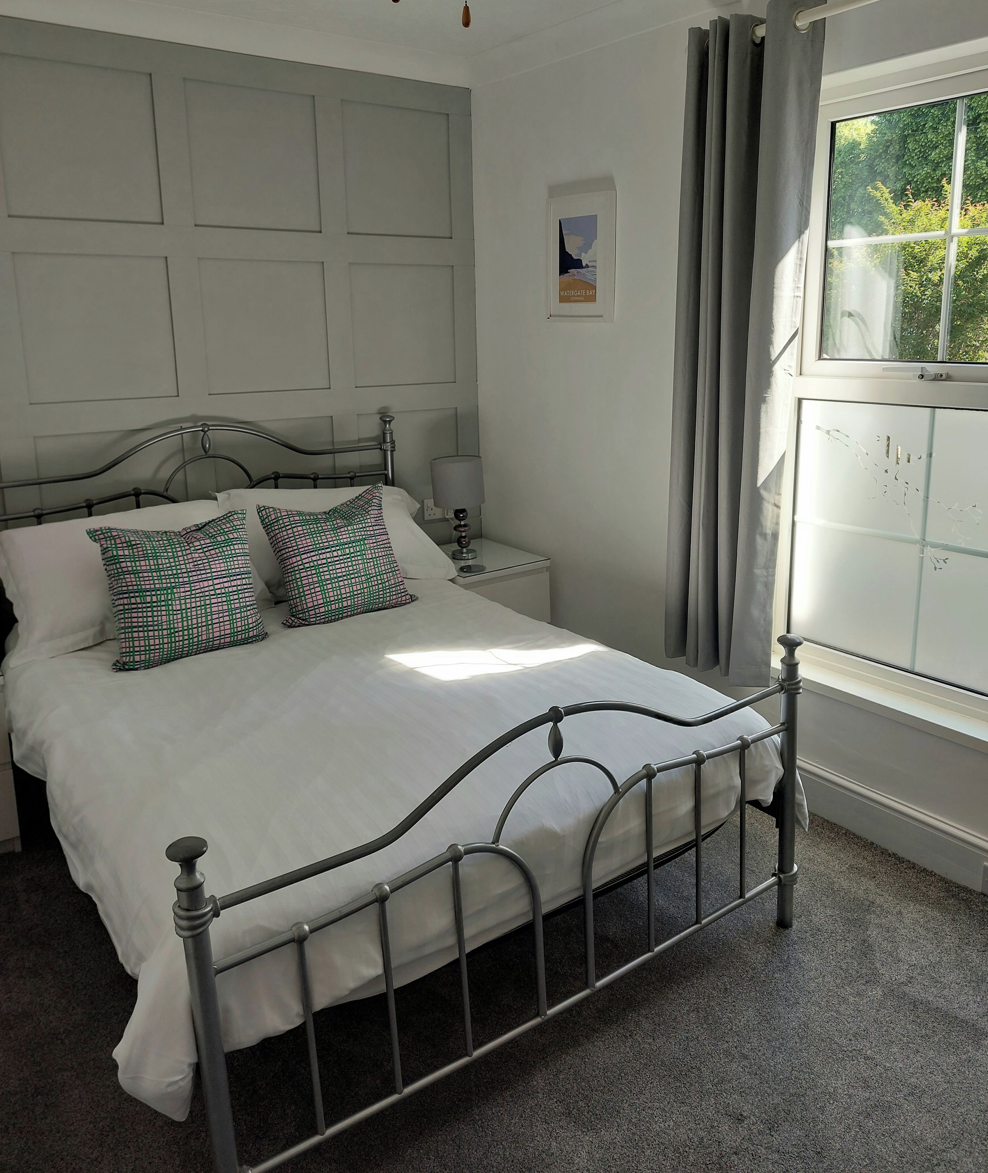 A bedroom with a metal bed frame, white bedding, a nightstand with a lamp, and a window with curtains.