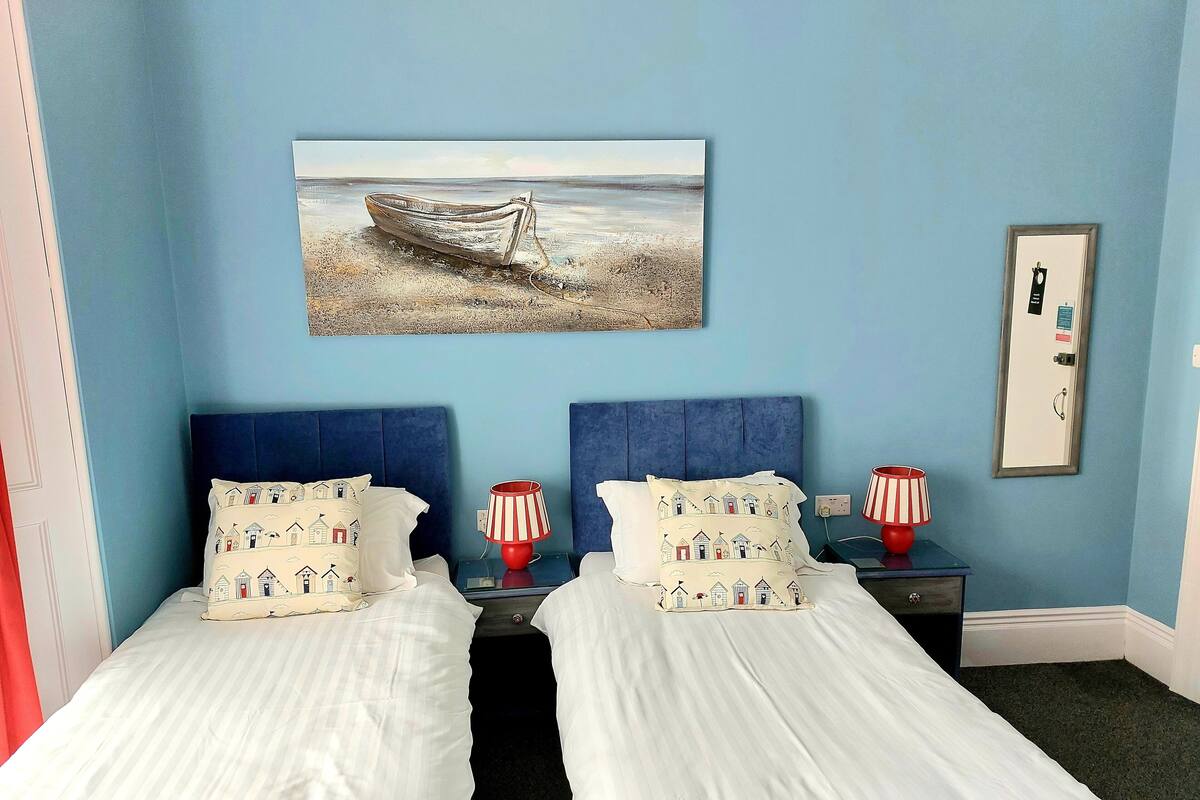 A room with two beds, a painting of a boat on the wall, and a door with a lock.