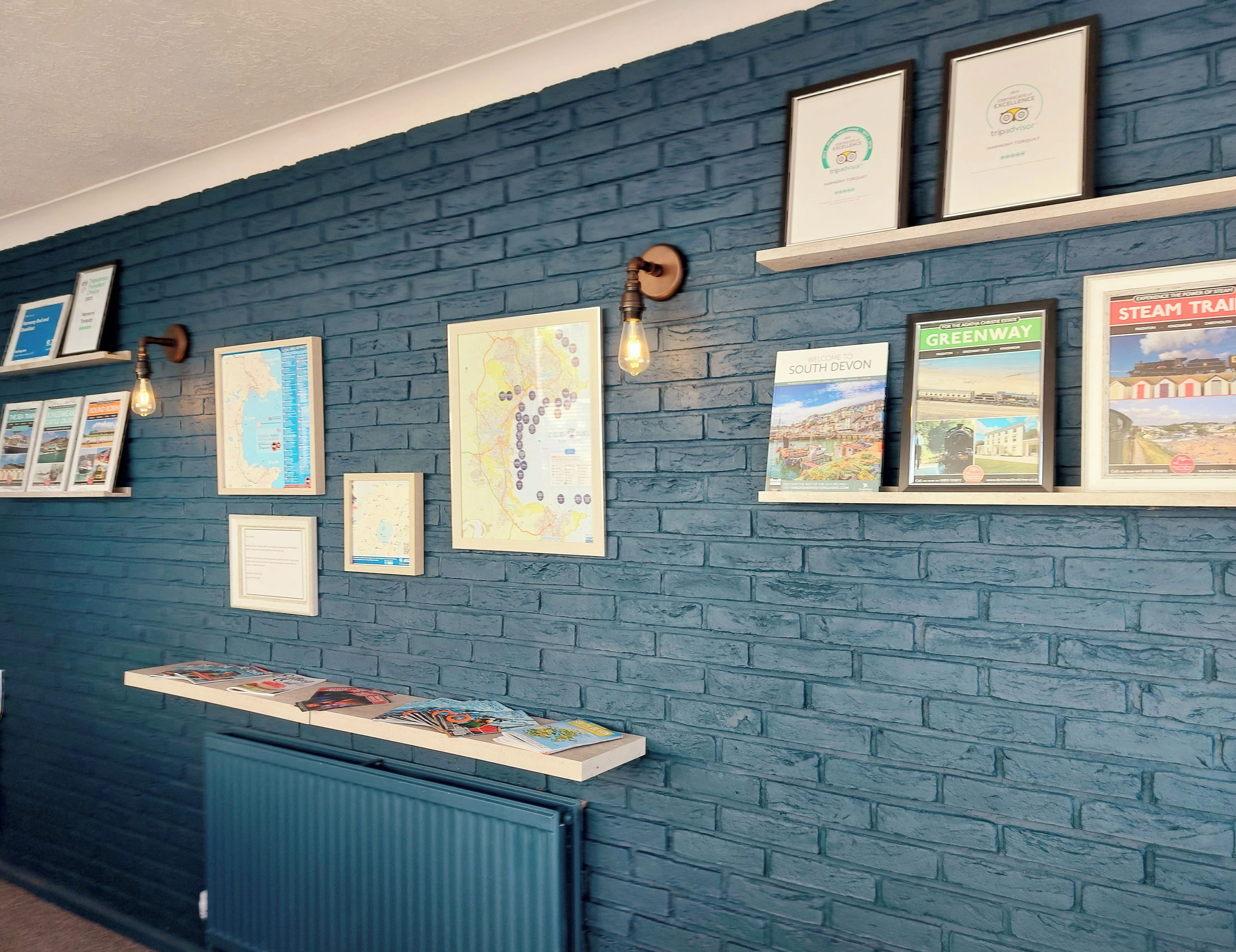 A wall with framed maps and travel guides, a radiator, and a shelf with brochures.