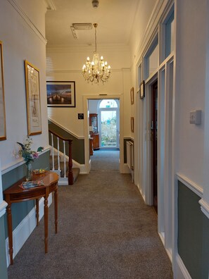 A hallway with a chandelier, framed pictures, a vase with flowers, and a staircase. - Harmony Guest House (Torquay)