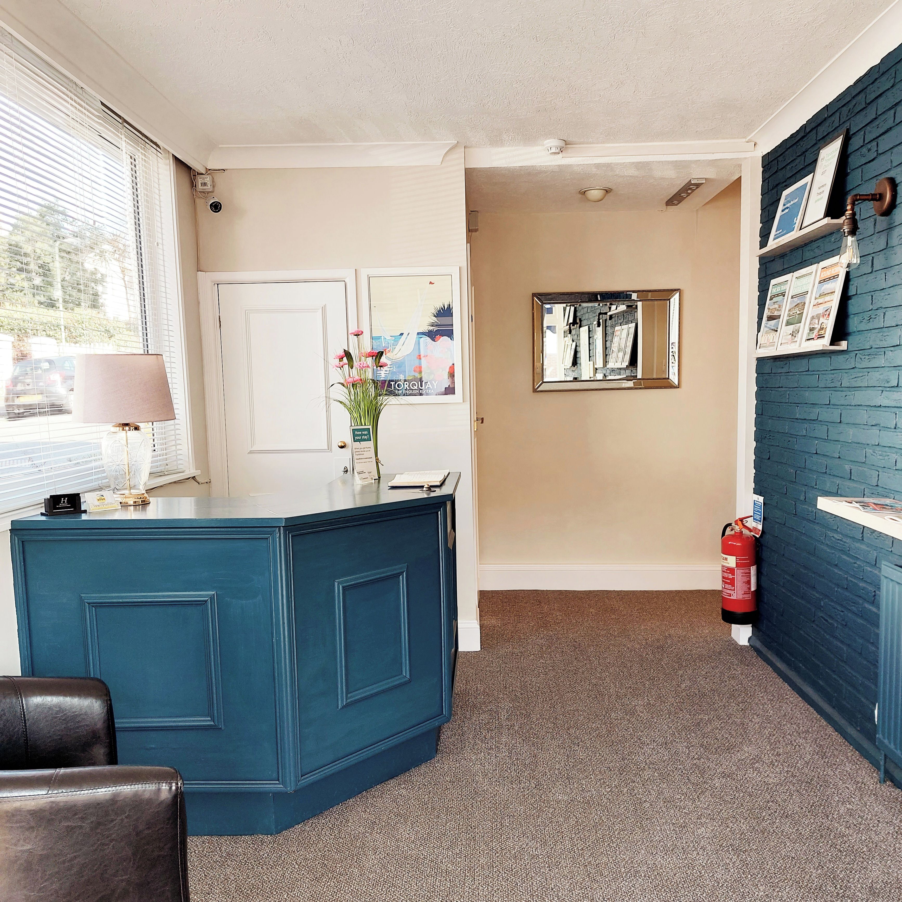 A room with a blue accent wall, a reception desk, a door, a framed mirror, and a fire extinguisher.