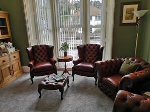 A room with two leather armchairs, a leather sofa, a wooden sideboard, and a small round table with a plant. - Harmony Guest House (Torquay)