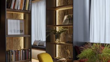 A modern living room with a bookshelf, a yellow armchair, and a window with curtains.