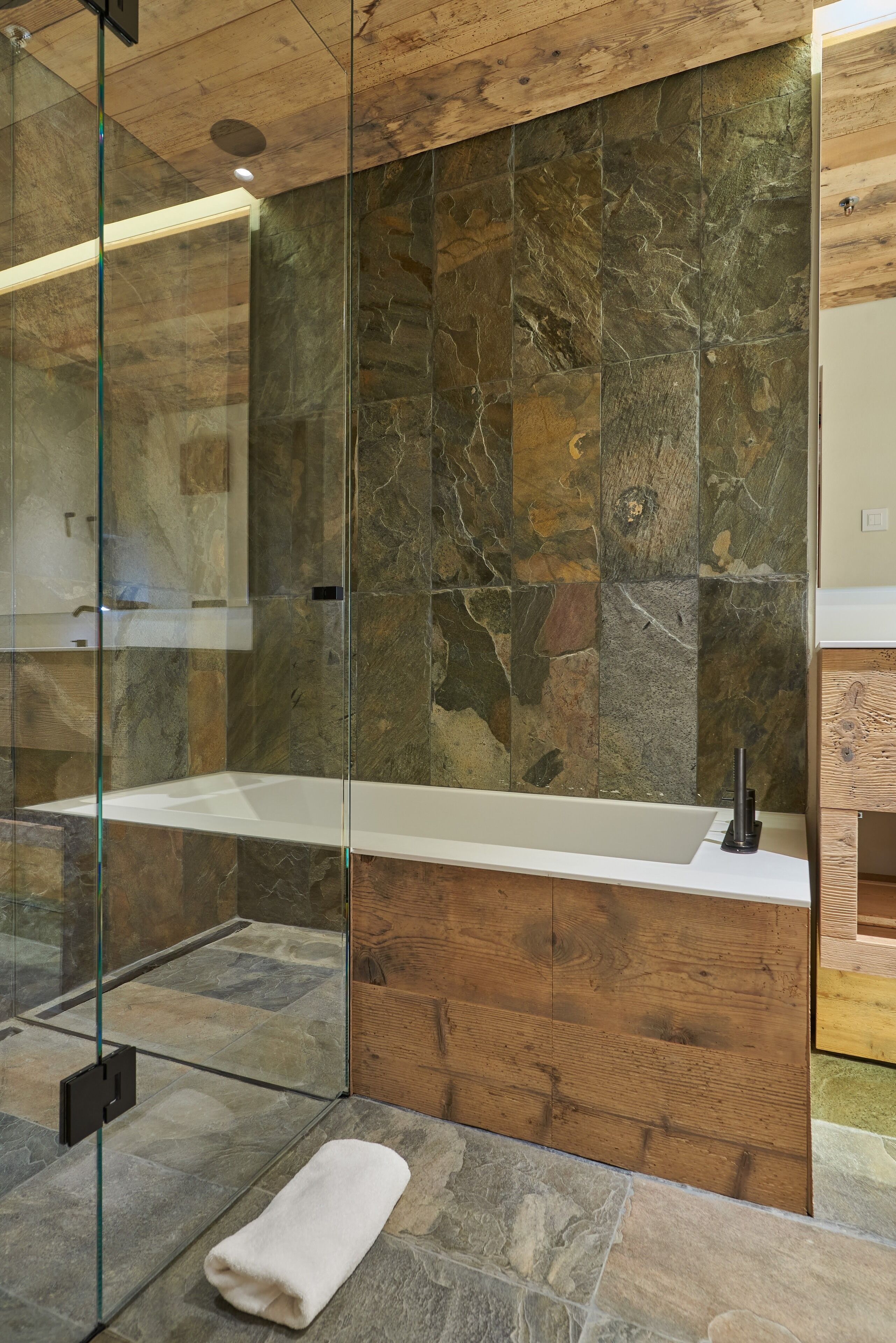 Ein modernes Badezimmer mit einer Steinwand, einer Glaskabinedusche und einem Holzanfangsschrank.