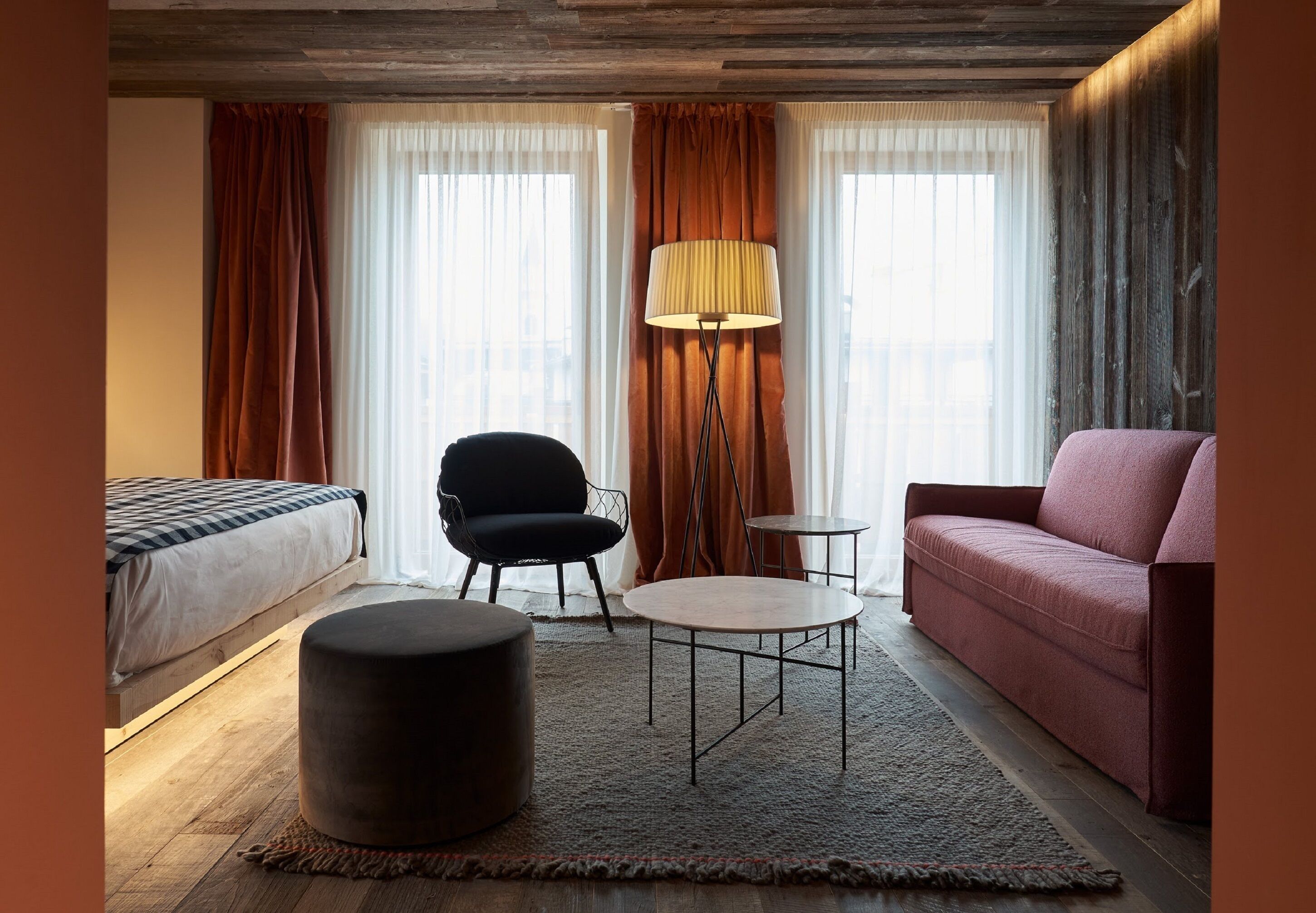 Et hotelværelse med en seng, en sort stol, et rundt bord, en sofa og en gulvlampe.