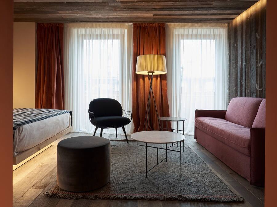 Habitación de hotel con cama, una silla negra, una mesa redonda, un sofá y una lámpara de pie.