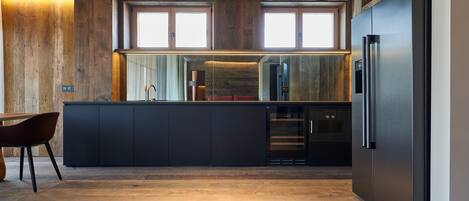 A modern kitchen with dark cabinetry, a stainless steel refrigerator, and a wooden ceiling.