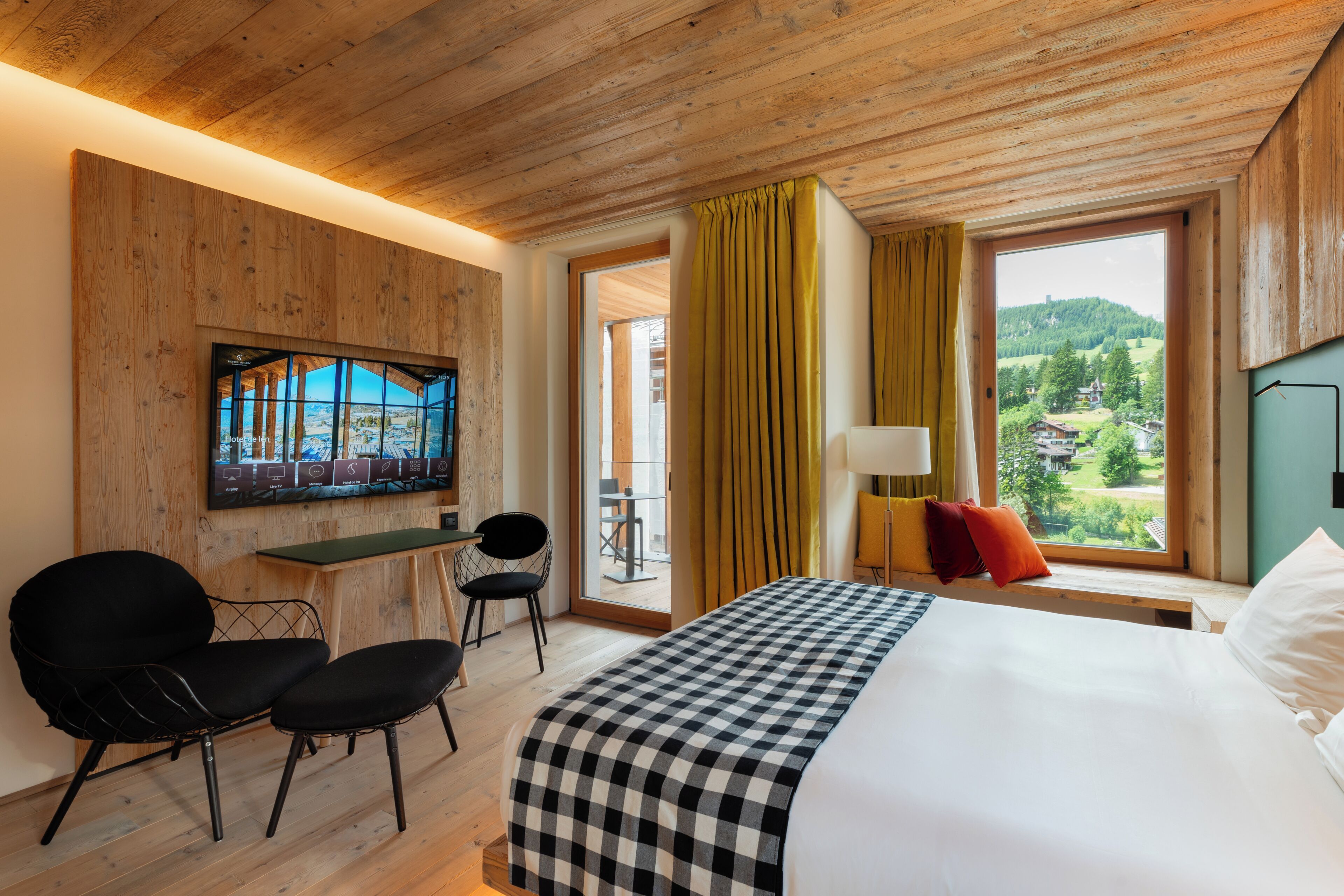 A hotel room with a bed, a desk, two chairs, a TV, and a window with curtains.