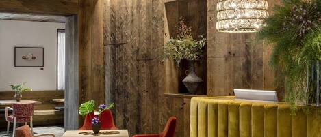 A modern interior with a wooden ceiling, a yellow upholstered reception desk, red chairs, and a chandelier.
