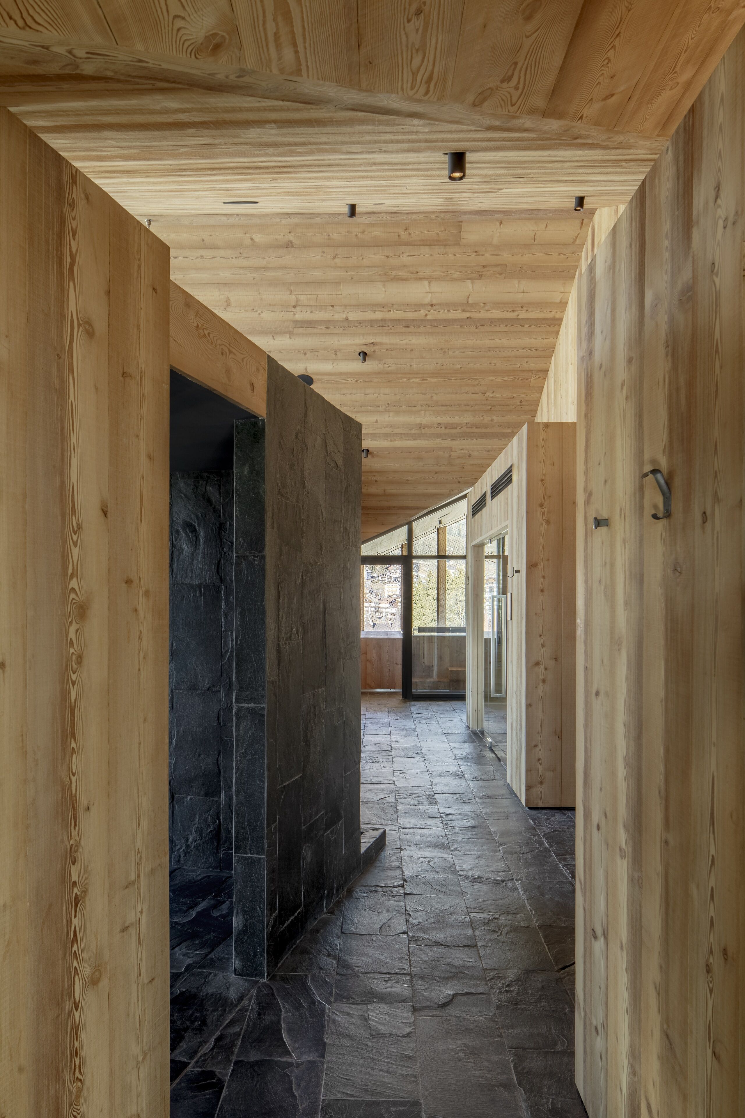 A corridor with wooden walls and a stone floor, leading to a glass door.
