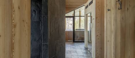 A corridor with wooden walls and a stone floor, leading to a glass door.