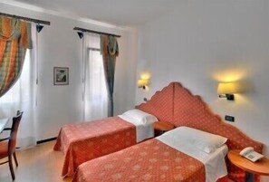 A hotel room with two single beds, a small table, a chair, and a door with curtains. - Antica Locanda Il Sole (Castel Maggiore)